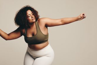Self-confident woman dancing in a studio, enjoying herself as she finds her flow. Woman in fitness clothing expressing her confidence and self-assurance in this effortless body movement.